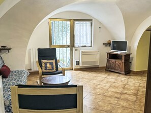 Ein gemütliches Wohnzimmer mit einem runden Tisch, einem Sessel mit Kissen, einem Fernseher auf einem Holzboden und einer Heizung.