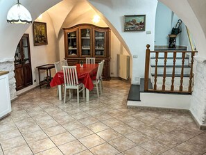 Ein Essbereich mit rotem Tischlein, weißen Stühlen, einer Holzkabine mit Glastüren und einer Treppe mit Holzgeländer.