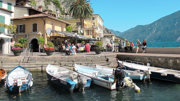 A coastal town with boats docked at the harbor, a café with outdoor seating, and buildings with balconies overlooking the sea. - "Casa Rita AP. 1 - Gardasee". by Interhome (Limone sul Garda)