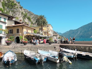 A coastal town with boats docked at the harbor, a café with outdoor seating, and buildings with balconies overlooking the sea. - "Casa Rita AP. 1 - Gardasee". by Interhome (Limone sul Garda)