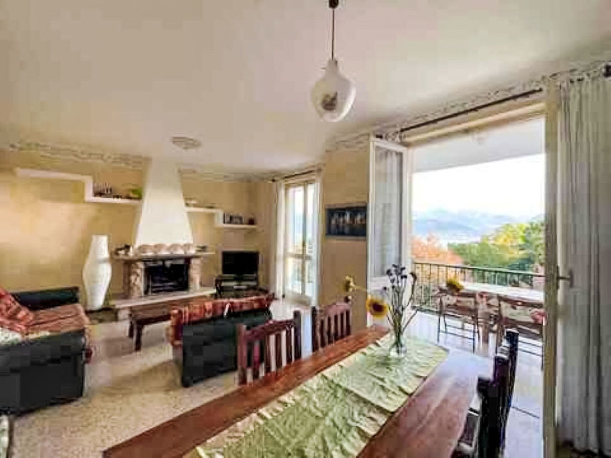 A spacious living room with a fireplace, a dining table, and a balcony with a view.