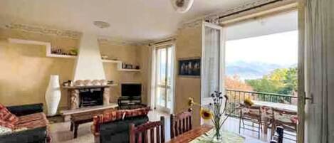 A spacious living room with a fireplace, a dining table, and a balcony with a view.