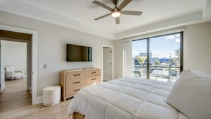 Quarto com cama grande, ventilador de teto, televisão, cómoda de madeira e vista para a cidade.