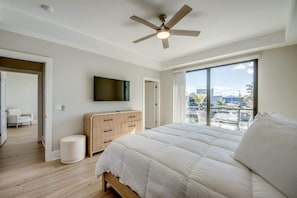 A bedroom with a large bed, a ceiling fan, a TV, a wooden dresser, and a view of the city. - 501 Palermo Luxe Canalfront Home with Private Pool (Fort Myers Beach)