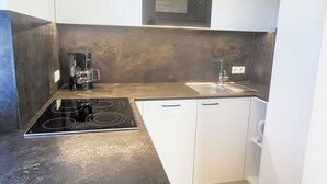 Eine kompakte Küche mit Einbau-Mikrowelle, Kaffeemaschine, Spüle und Kochfeld.
