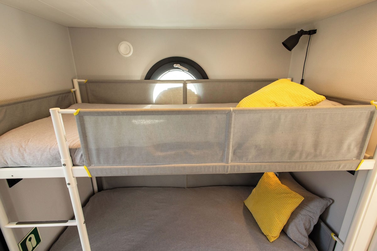 Ein Stockbett mit Fenster darüber und einer Lampe zur rechten Seite.