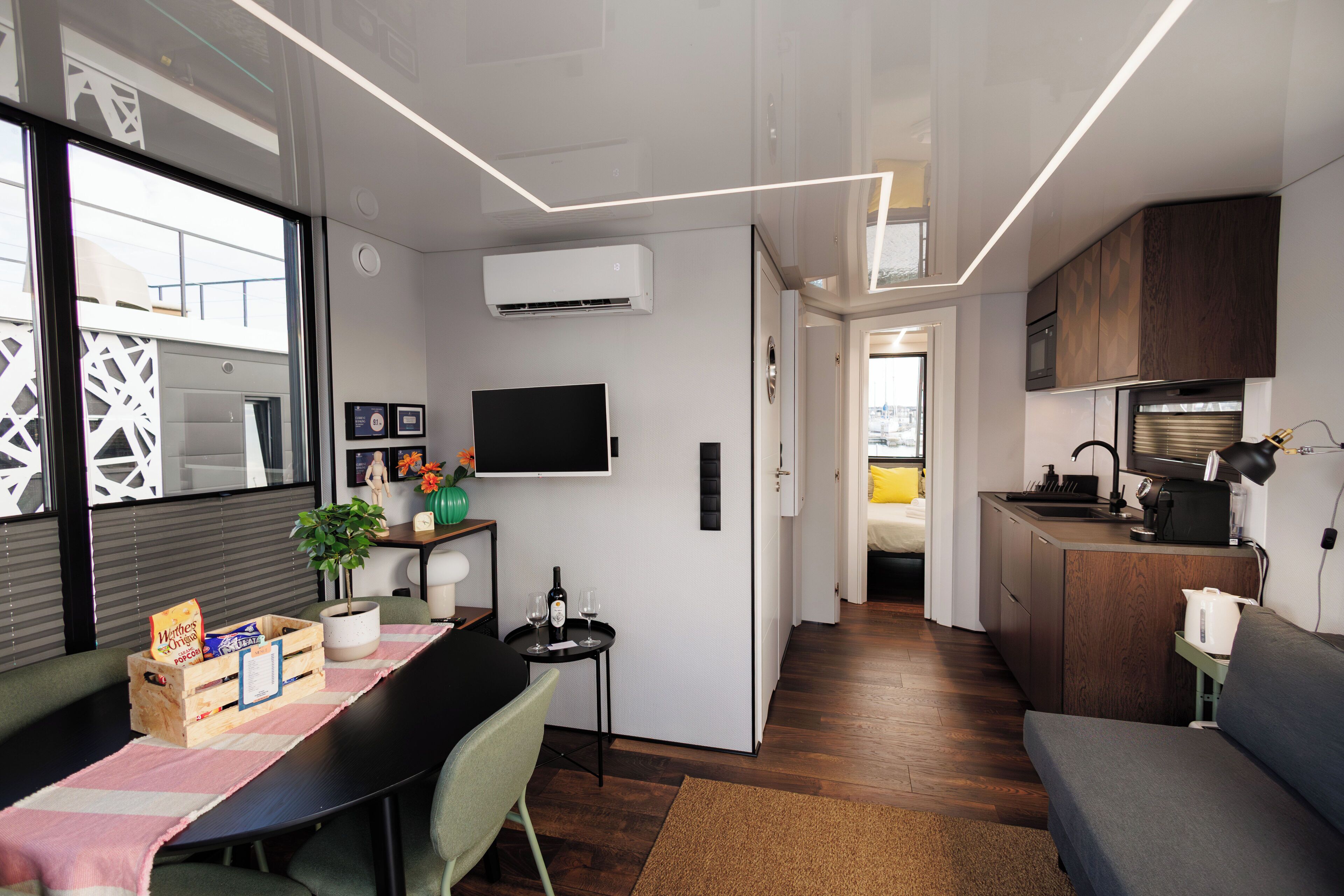 A compact living space with a dining area, kitchenette, and a TV mounted on the wall.