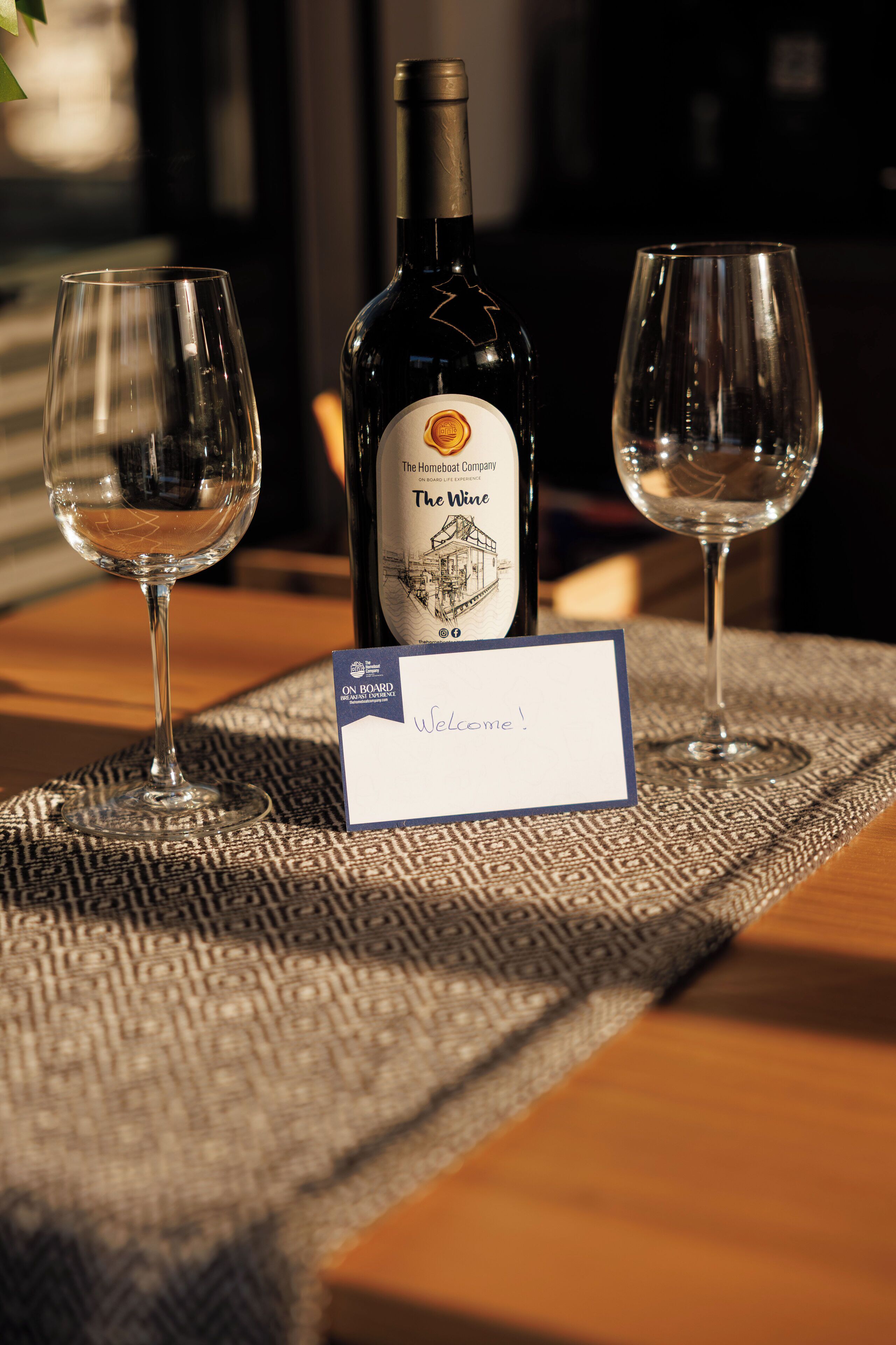 Een fles wijn en twee glazen op een tafel met een welkomstbord.