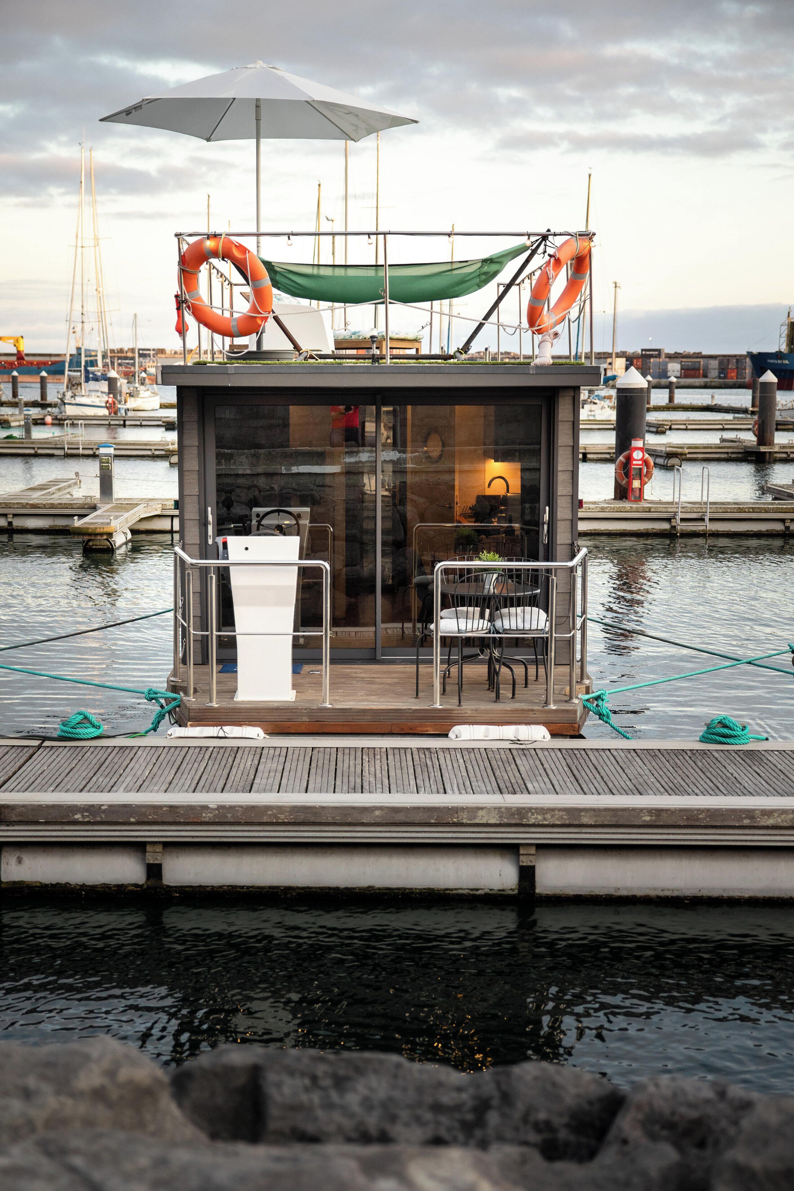 A small, enclosed dock area with a table and chairs, a hammock, and life rings.