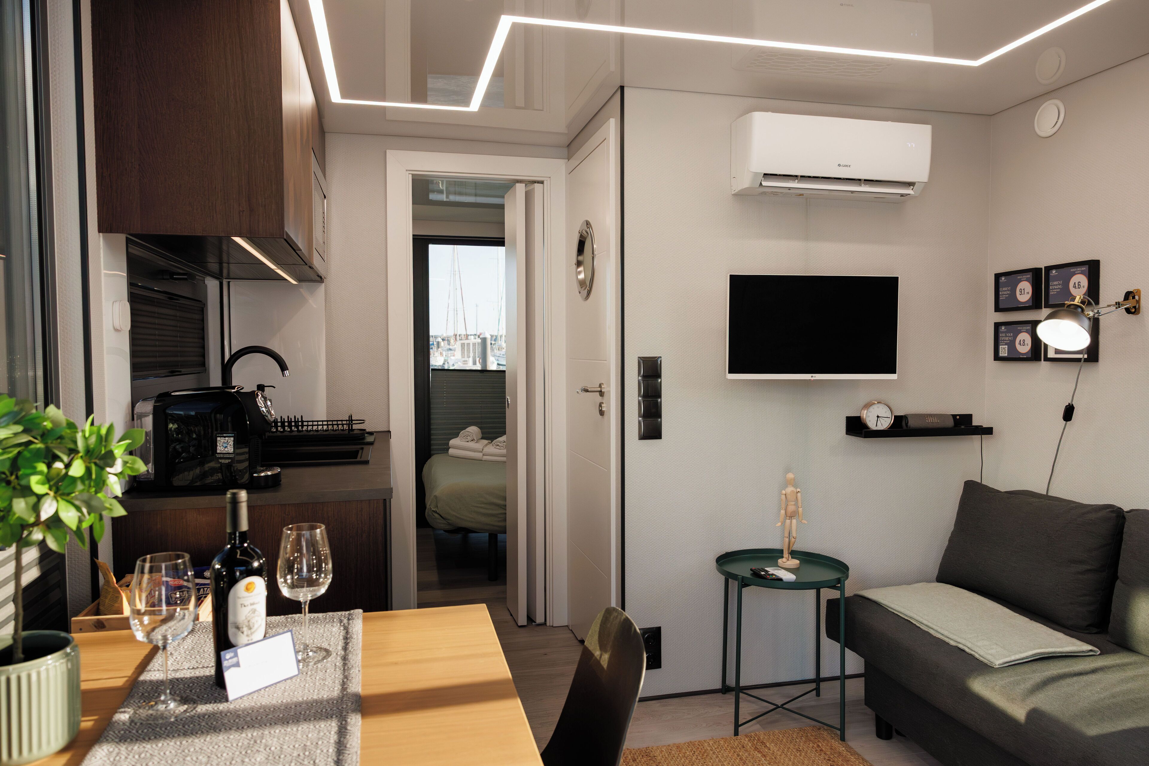 A modern living room with a sofa, a TV mounted on the wall, and a dining area with a table and chairs.