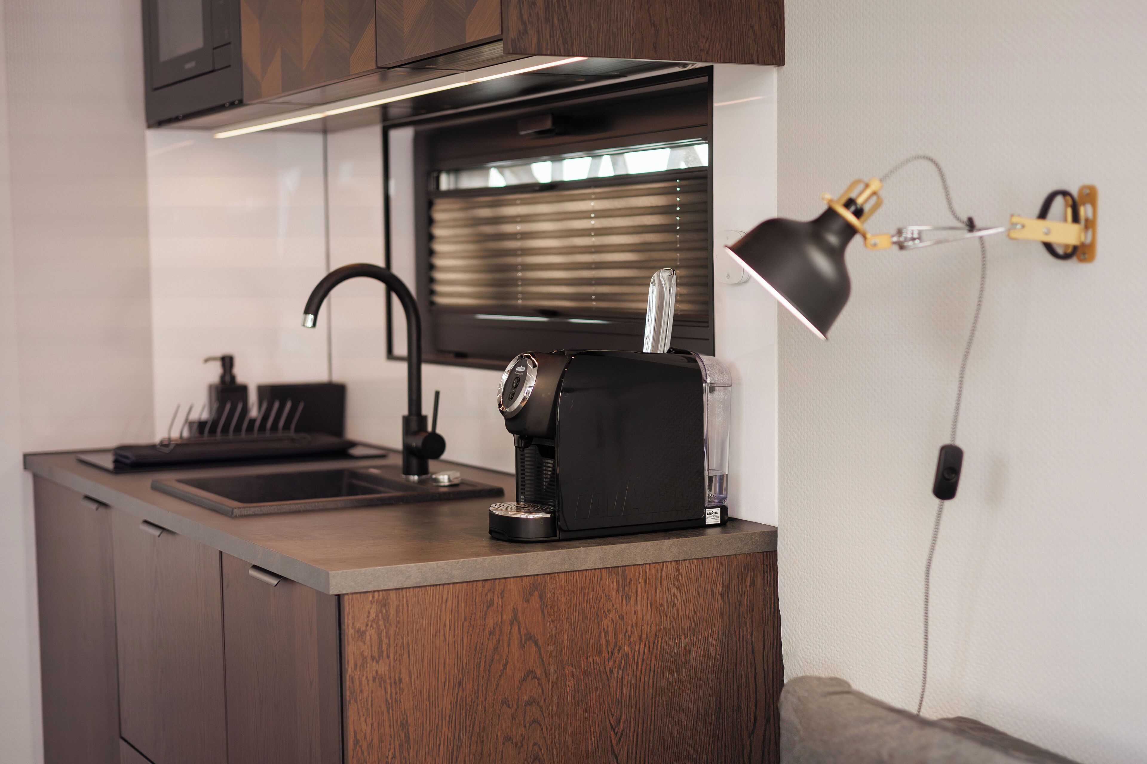 Een compacte keuken met een modern design, inclusief een geïntegreerde spoelbak, een koffieapparaat en een wandlamp.
