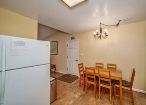 Una cocina funcional con refrigerador, una mesa de comedor con sillas y una araña.