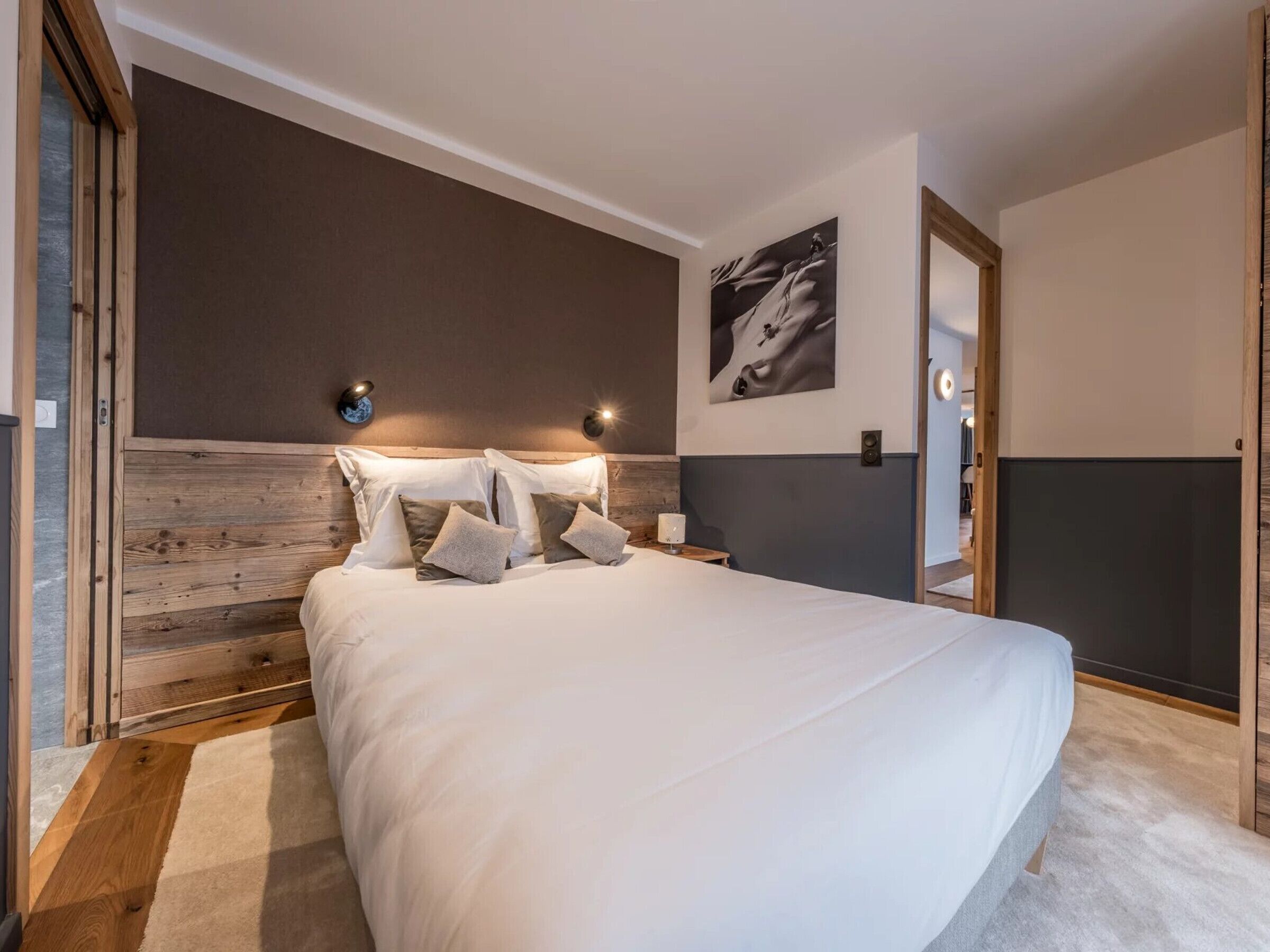 Una camera da letto moderna con una testiera in legno, un letto grande con biancheria bianca, una lampada a parete e un quadro incorniciato.