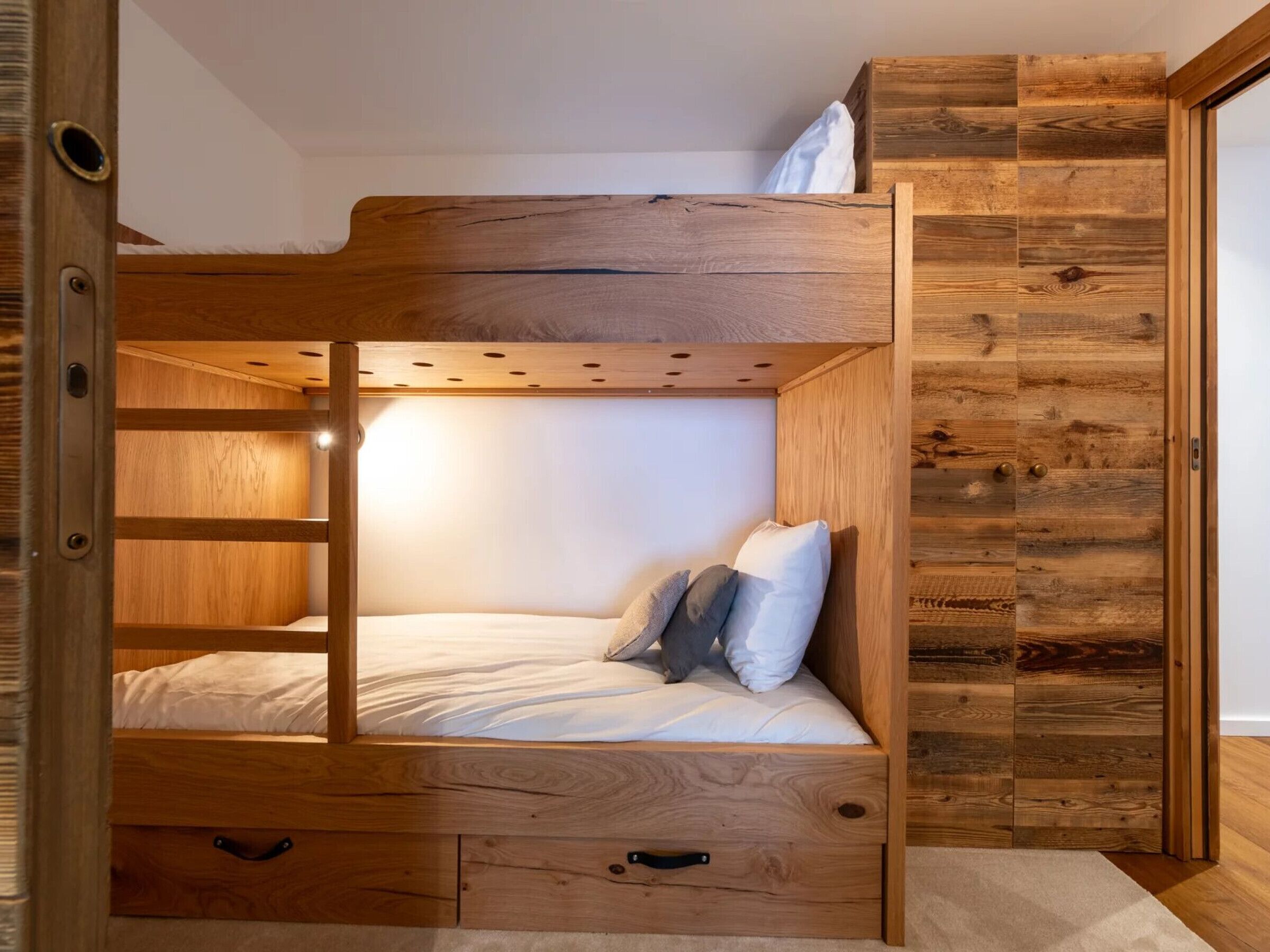 Un lit superposé avec une structure en bois, un tiroir coulissant et une tête de lit dotée d’une étagère intégrée.