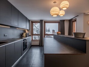 Une cuisine moderne avec des meubles de couleur sombre, un four encastré et une grande fenêtre donnant sur un paysage enneigé.