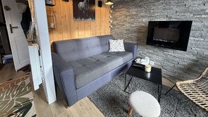 Moderni olohuone, jossa on harmaa sohva, pieni pyöreä pöytä, rottinkituoli, takka ja seinälle kiinnitetty peuranpää.