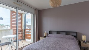 Un dormitorio con cama, mesita de noche, lámpara colgante y puerta corredera de vidrio que da a un espacio exterior con mesa y sillas.