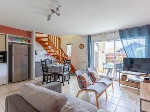 A modern living room with a sofa, two armchairs, a dining table with chairs, a kitchen area with a refrigerator, and a staircase leading to another level. - 2* Apartment with terrace near lake, 4 guests (Biscarrosse)