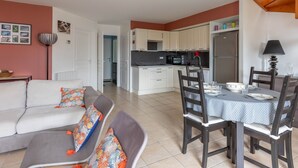 Un espacio habitable compacto con kitchenette, comedor y zona de estar con sofá y sillones.
