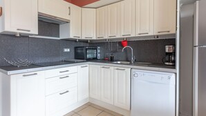 Una cocina con armarios blancos, encimera negra, microondas, cafetera y lavavajillas.