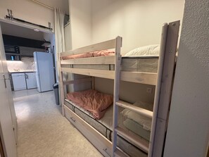 Une chambre avec des lits superposés, et une petite cuisine en arrière-plan.