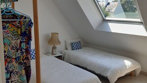 Une chambre avec deux lits, une table de chevet, une lampe et une fenêtre donnant sur des immeubles.