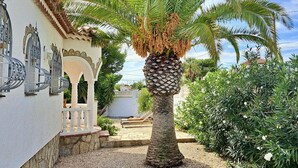 A courtyard with a palm tree, a white building with arches, and a stone wall. - Spacious Villa in Miami Platja (Miami Playa)