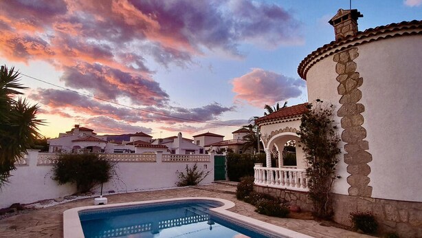 A swimming pool with a stone wall and a building with a tiled roof. - Spacious Villa in Miami Platja (Miami Playa)