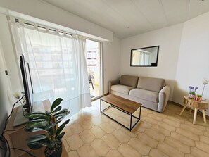 Ein Wohnzimmer mit einer Couch, einem Couchtisch, einem Fernseher und einer Topfpflanze.