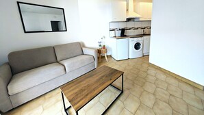 A modern living room with a sofa, a wooden coffee table, a washing machine, and a kitchen area. - Renovated Studio - 5 Pers - Sea View - Canet-en-Roussillon (Canet-en-Roussillon)
