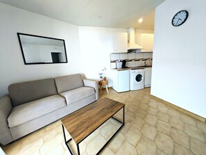 Ein modernes Wohnzimmer mit einer Couch, einem Holztisch, einer Waschmaschine und einer Küchenzeile.