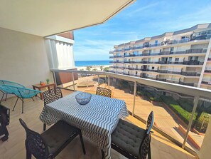 Ein Balkon mit Tisch und Stühlen, mit Blick auf einen Strand und ein mehrstöckiges Gebäude.