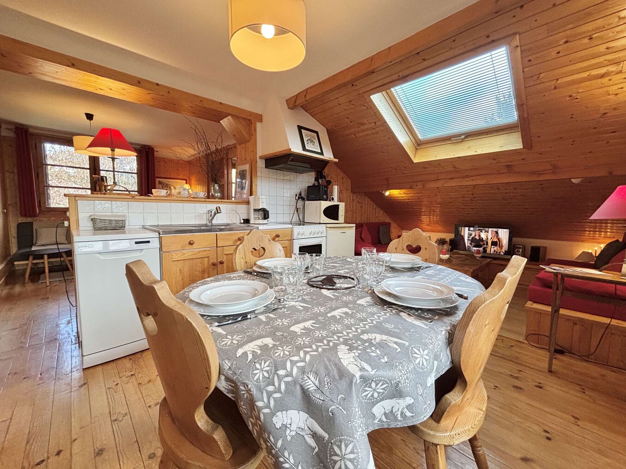 Una cocina acogedora y rústica con vigas de madera, un comedor con mantel estampado, y un televisor en la sala.
