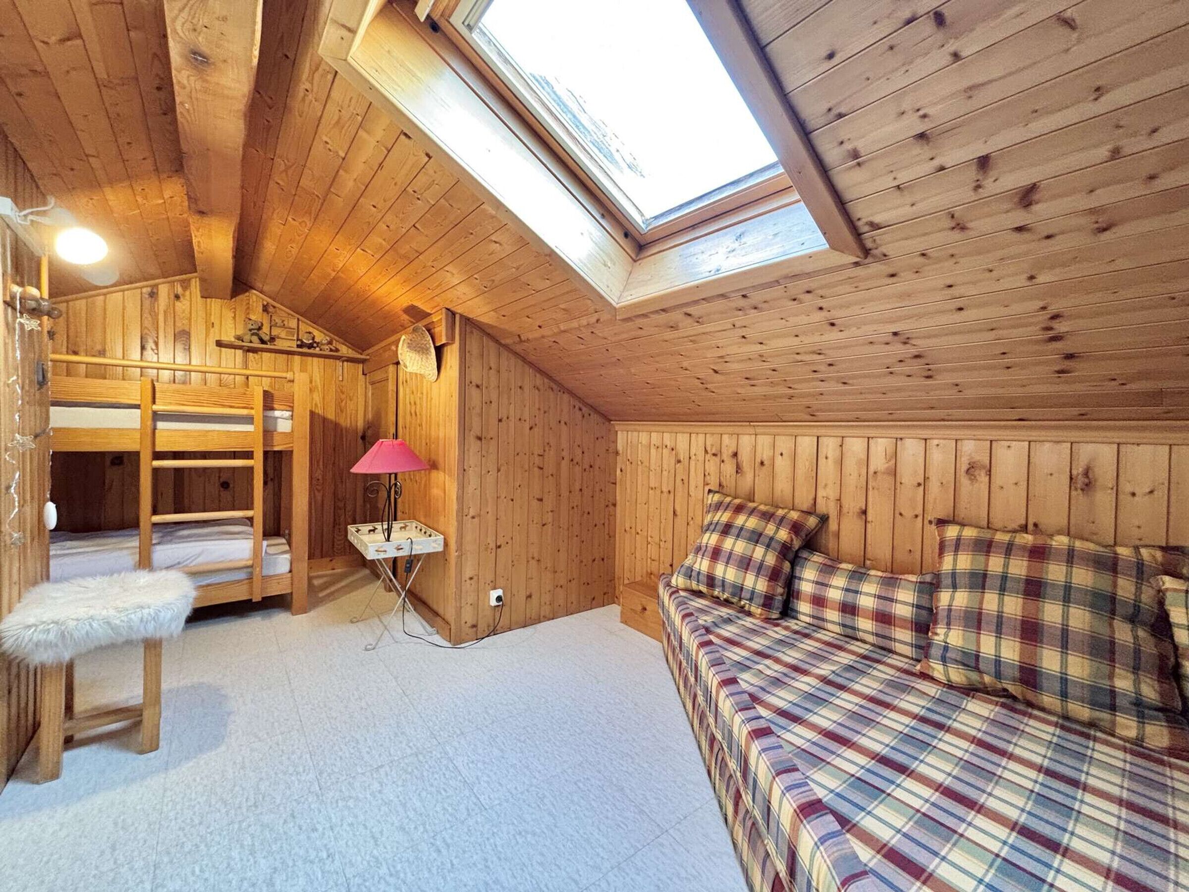 A cozy attic bedroom with a bunk bed, a small desk with a lamp, and a plaid bedspread.