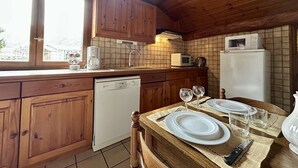 A kitchen with wooden cabinets, a dishwasher, a microwave, and a refrigerator. There is a window providing natural light and a view of the outside. - Charming 3-Room Apartment, Sleeps 4 in La Salle-les-Alpes (La Salle-les-Alpes)
