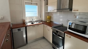 A compact kitchen with a dishwasher, oven, microwave, and a window with a view of the sea. - Charming 2-bedroom apartment with terrace and parking in Roses (Roses)