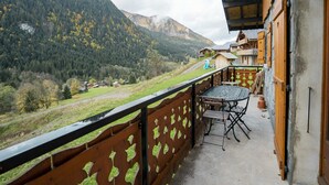 A balcony with a table and chairs, overlooking a mountainous landscape with houses in the distance. - Charming Chalet for 5 Guests in Châtel (Châtel)