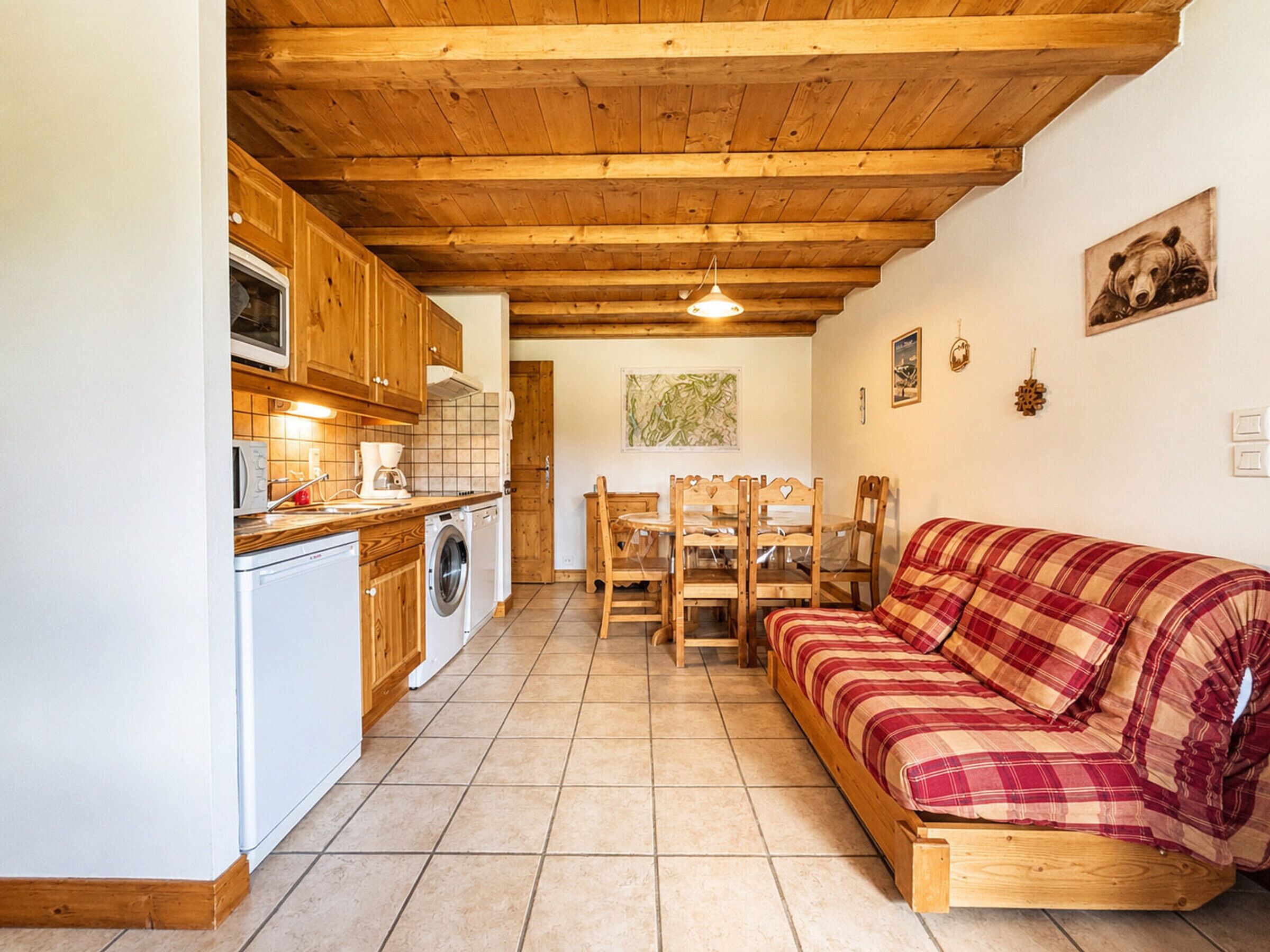 Een compacte keuken met houten keukenkastjes, een wasmachine en een eethoek met een houten tafel en stoelen.