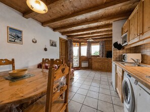 A wooden interior with a dining table, chairs, a washing machine, and a kitchen area. - Cozy apartment near Cernix with balcony and parking (Crest-Voland)