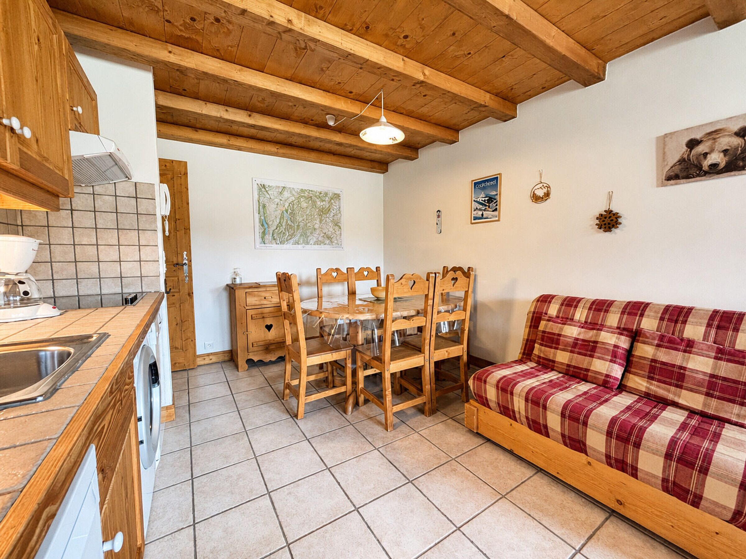 Una cucina con mobili in legno, un tavolo da pranzo con sedie, un divano rosso a quadri e un pavimento piastrellato.