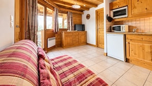 A cozy wooden cabin with a sofa, kitchenette, and a window with curtains. - Cozy apartment near Cernix with balcony and parking (Crest-Voland)