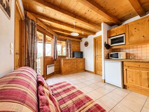 A cozy wooden cabin with a sofa, kitchenette, and a window with curtains. - Cozy apartment near Cernix with balcony and parking (Crest-Voland)