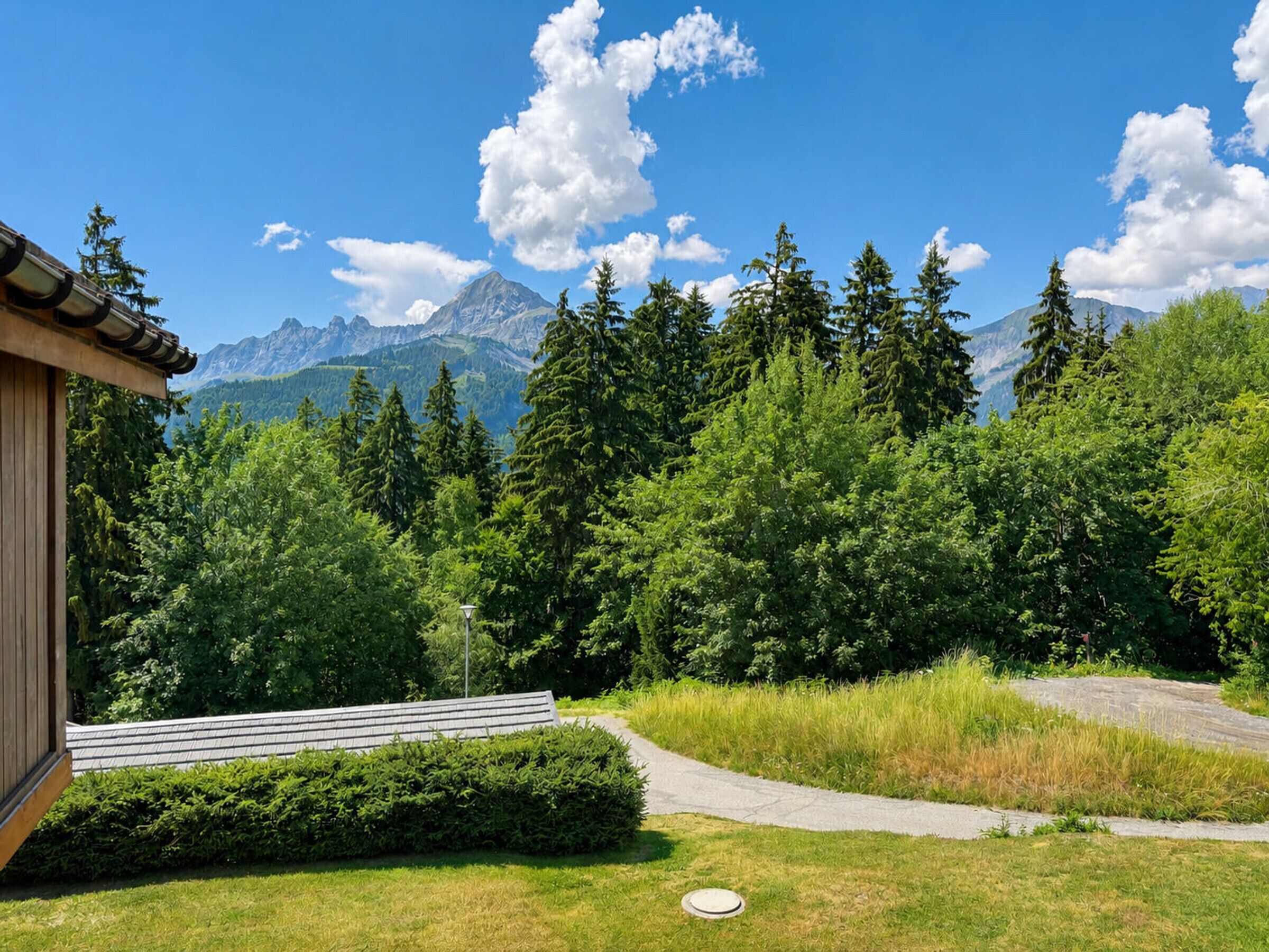 Blick auf Berge mit einem Pfad, der zu einem Gebäude führt, umgeben von dichtem Wald und Bergen.