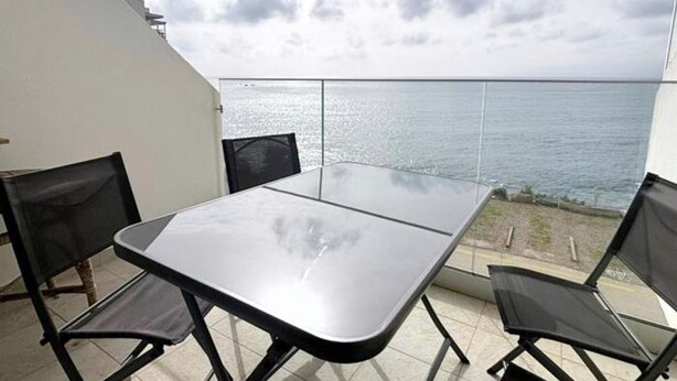 En balkon med et bord og stole, der kigger ud over vandet.