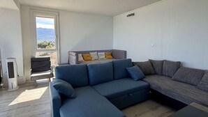 Ein modernes Wohnzimmer mit einer Eckcouch, einem kleinen Tisch und einem Fenster mit Blick ins Freie.