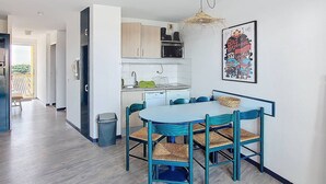 Cocina moderna con armarios blancos, microondas y lavamanos. Hay una mesa de comedor con sillas azules y una lámpara colgante.