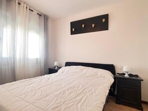 Ein Schlafzimmer mit einem Bett, zwei Nachttischen, einer Wandleuchte und einem Fenster mit Vorhängen.