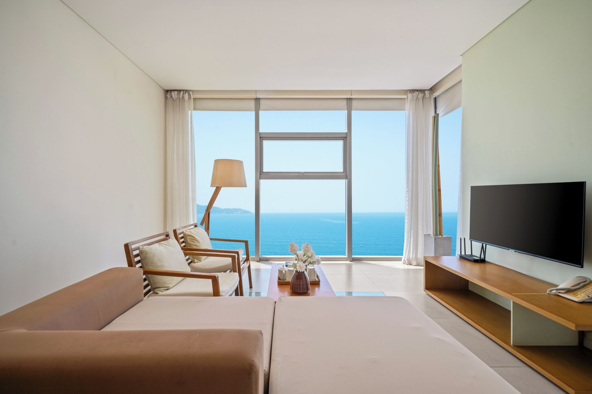 A hotel room with a large window, a bed, a sofa, a TV, and a lamp.