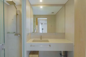 Un bagno moderno con box doccia in vetro, lavabo bianco con specchio sopra e una porta che dà su un'altra stanza.