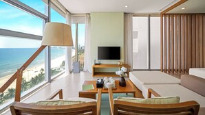 A modern living room with a large TV, wooden furniture, a coffee table, and a view of the beach. - Signature Luxury Village (Da Nang)